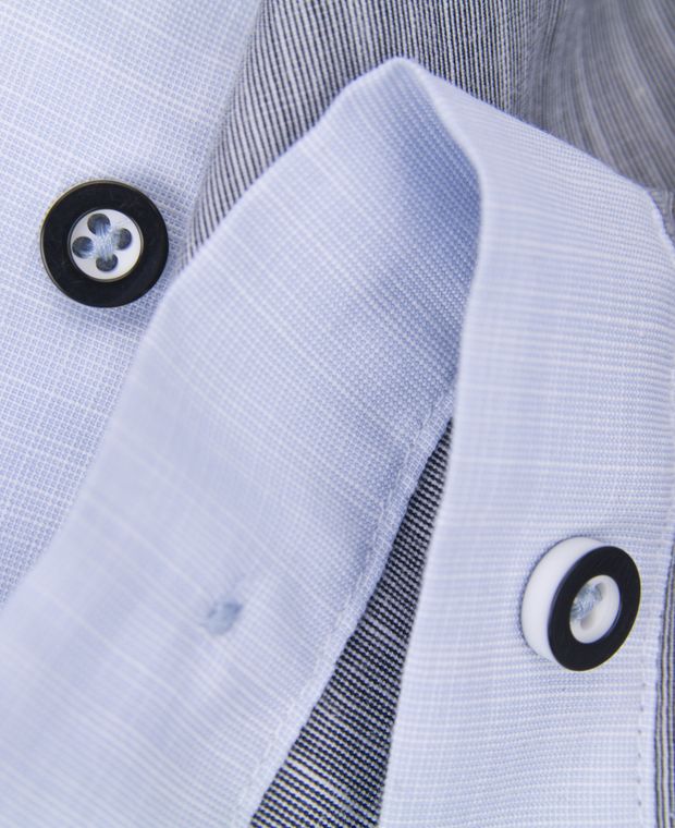 Close-up of light blue shirting fabric at a collar with dark-rimmed buttons