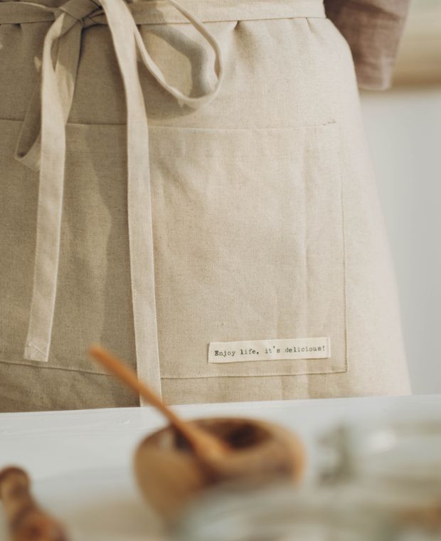 Natural cotton apron with ties and a front pocket carrying a small printed label