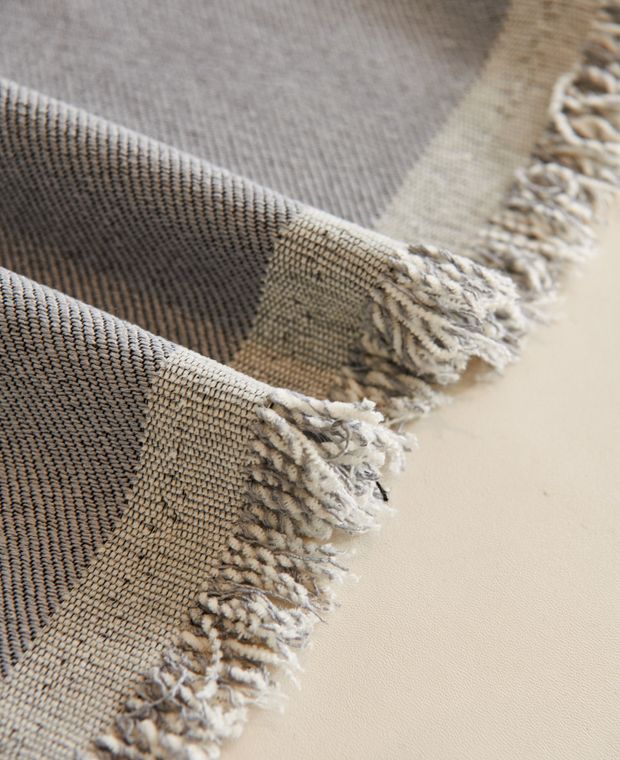 Folded grey woven cotton cloth with fringed edges on a cream surface