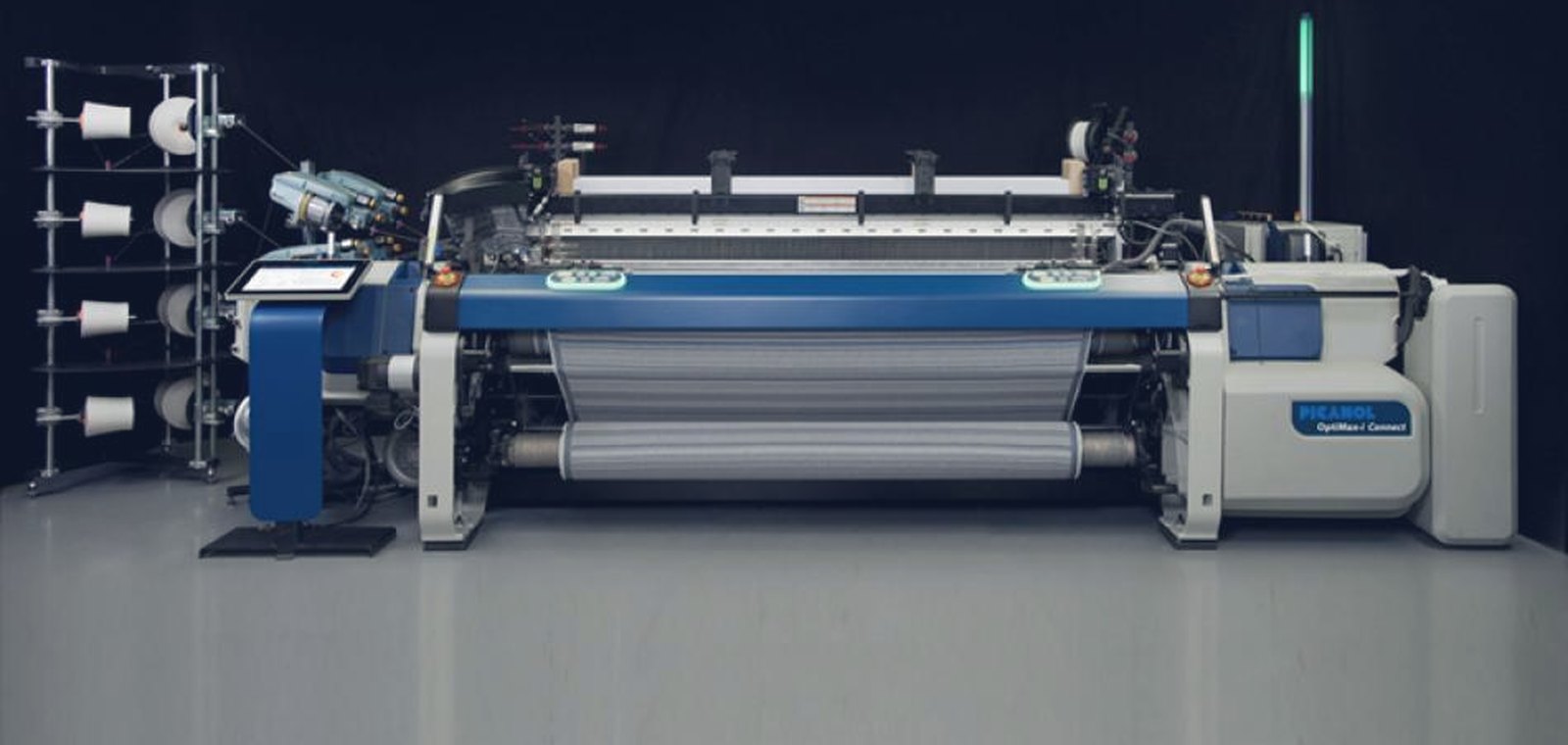 Modern rapier weaving loom with grey cloth on the take-up roller and yarn packages on a creel beside it